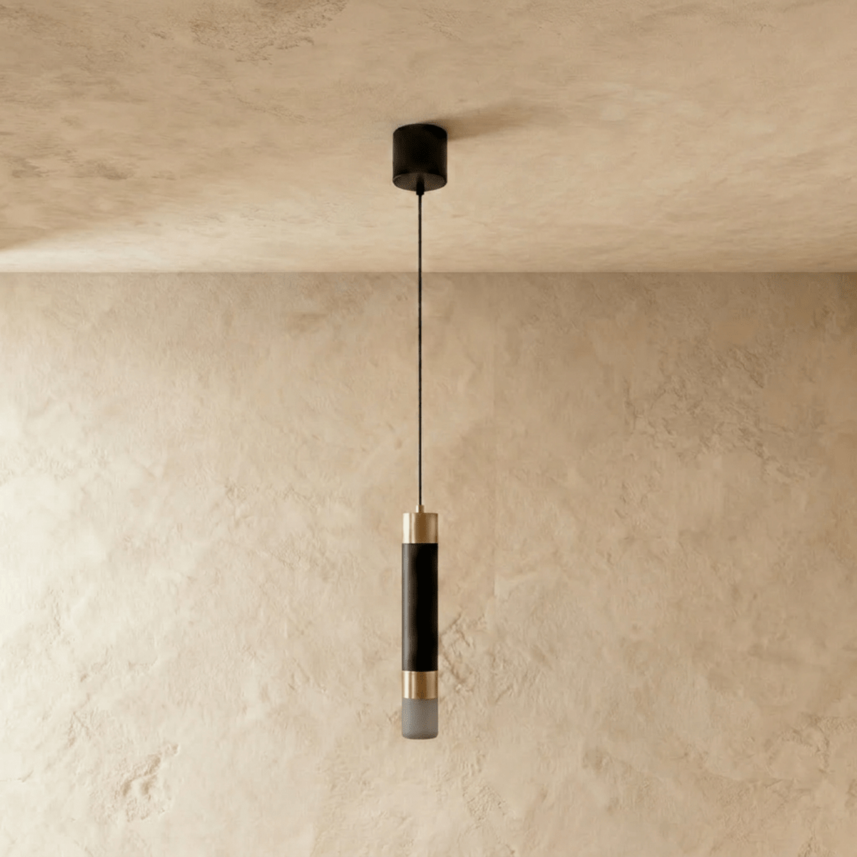 Clérachic single black cylinder pendant with gold-tone bands and a frosted end, switched off, on a limewash wall.