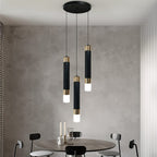 Clérachic round three-head pendant light, black cylinders with gold bands, hung over a round dining table by a grey wall.