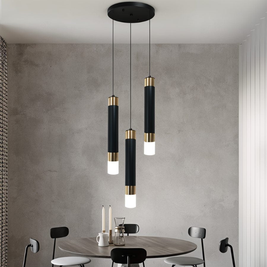 Clérachic round three-head pendant light, black cylinders with gold bands, hung over a round dining table by a grey wall.