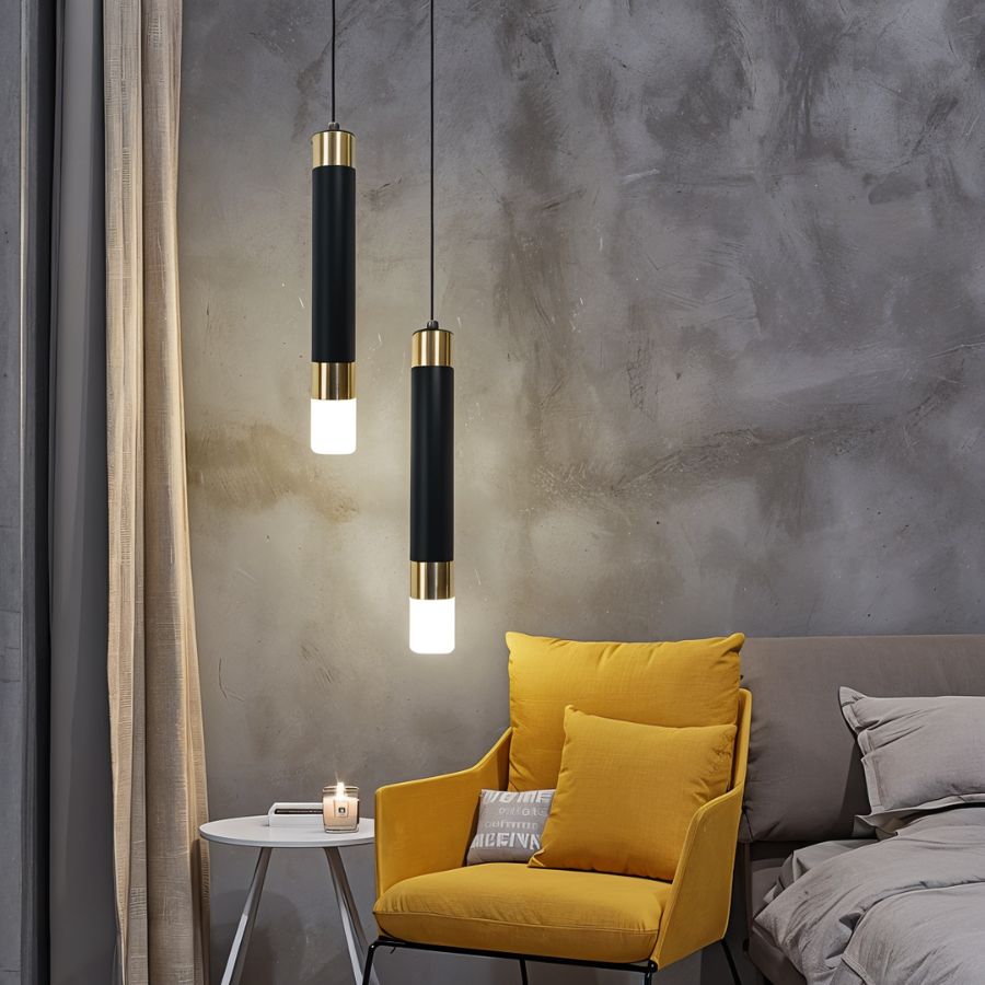 Clérachic two black cylinder pendants with gold-tone bands and glowing frosted bases beside a yellow armchair and grey wall.