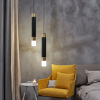 Clérachic two black cylinder pendants with gold-tone bands and glowing frosted bases beside a yellow armchair and grey wall.
