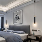 Clérachic pair of black cylinder pendants with gold bands hung on either side of a bed with a grey headboard.