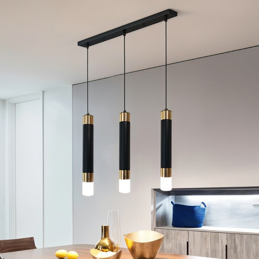 Clérachic long three-head pendant light, black gold-banded cylinders in a row above a dining table with gold bowls.