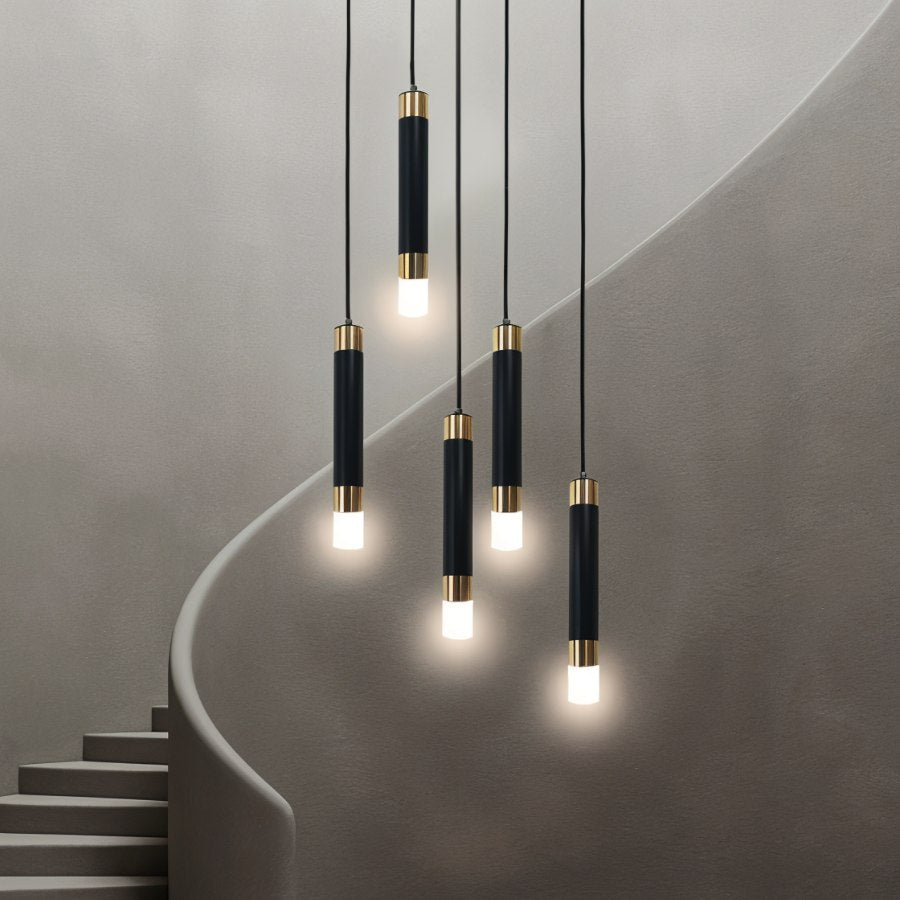 Clérachic cluster of five black gold-banded cylinder pendants glowing at different heights beside a curved staircase.