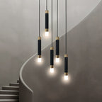 Clérachic cluster of five black gold-banded cylinder pendants glowing at different heights beside a curved staircase.