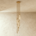 Clérachic three-head pendant in brushed gold with slim rods and clear glass teardrops, hung from a round canopy on a plaster wall.