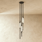 Clérachic three-head pendant in black with slim rods and clear glass teardrops, hung from a round black canopy on a plaster wall.