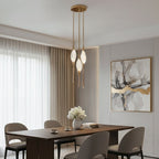 Clérachic three-head gold pendant with glowing glass teardrops above a walnut dining table, with sheer curtains and framed art.