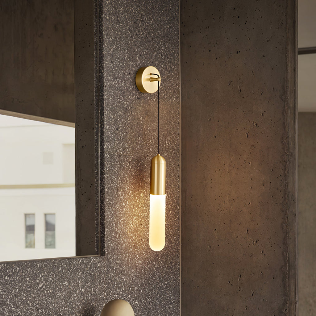 Lit brass Clérachic wall light against a rough dark stone pillar, its slim shade glowing warm beside a mirror with a window view.