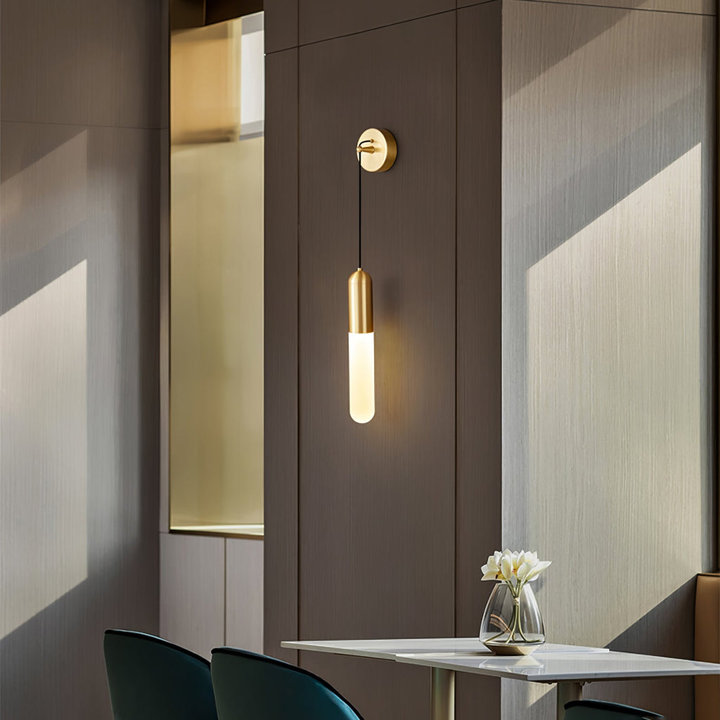 A Clérachic brass wall light on a dark panelled wall beside a gold-edged niche, with a table and a glass vase of flowers below.