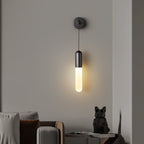 Black Clérachic wall light glowing warm on a grey wall above a sofa corner, with a small black animal figure on a side table.