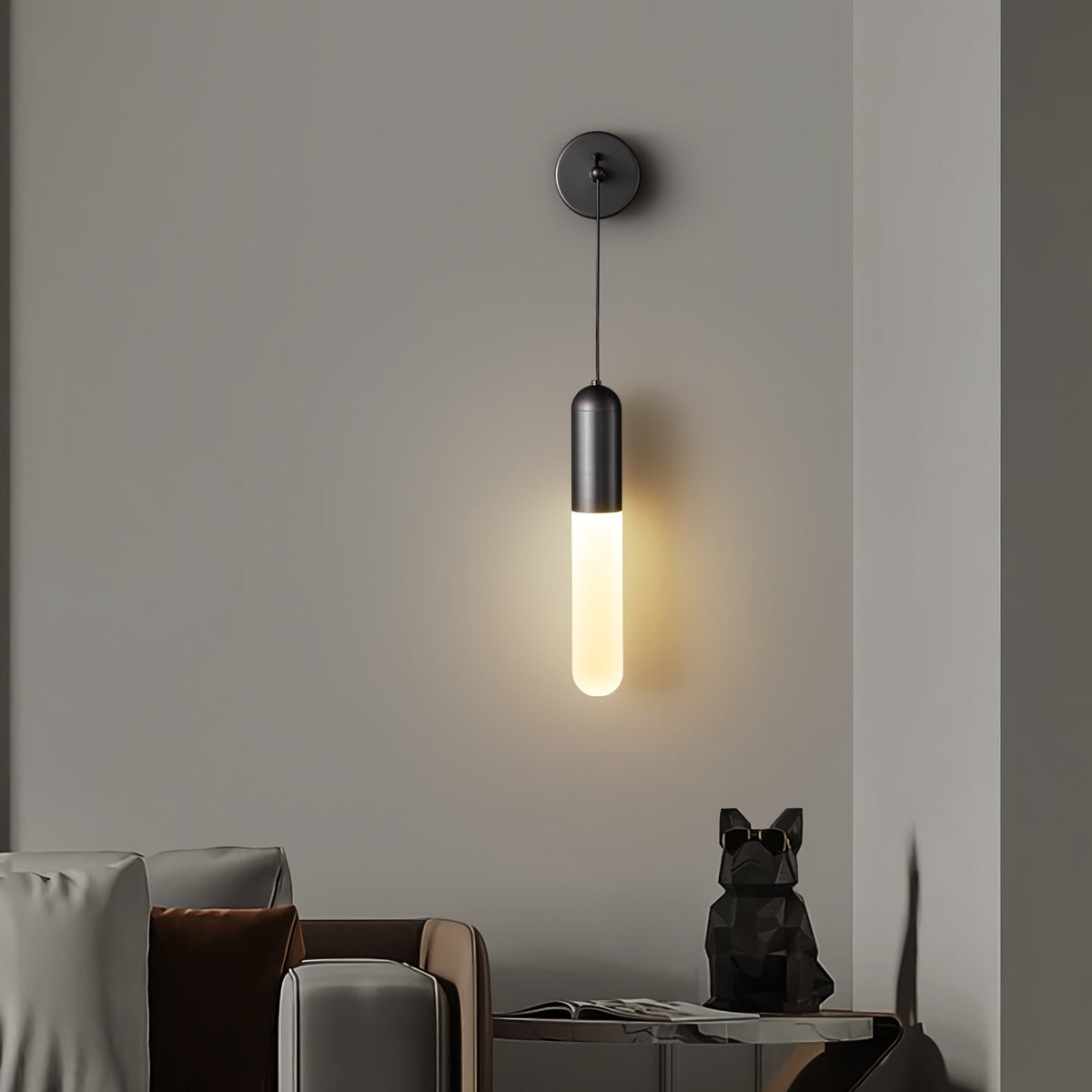 Black Clérachic wall light glowing warm on a grey wall above a sofa corner, with a small black animal figure on a side table.