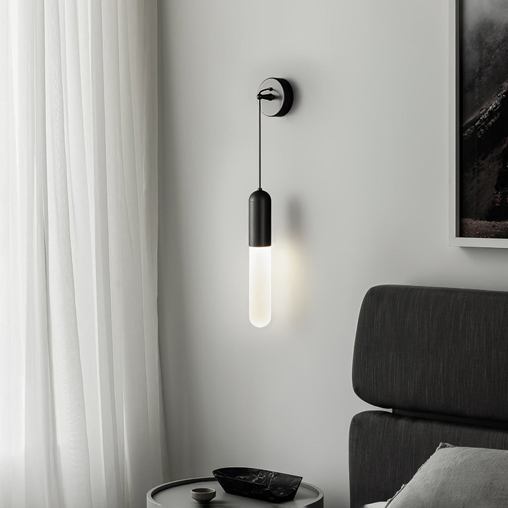 Black Clérachic wall light beside a sheer white curtain and a dark framed picture, with a charcoal bed headboard and a round bedside table.