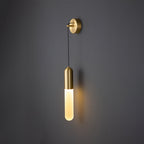 Brass Clérachic wall light lit warm on a dark grey wall, the slim cylinder shade casting a soft shadow to its side.