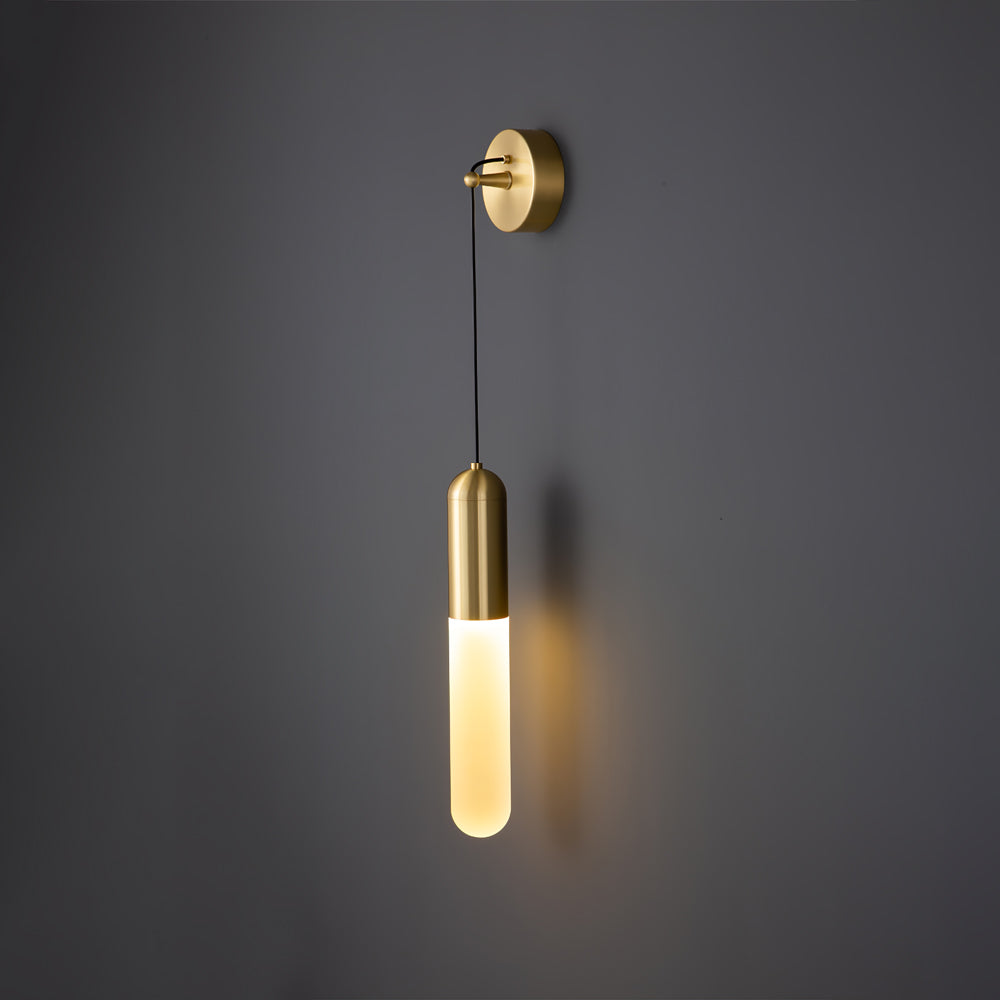 Brass Clérachic wall light lit warm on a dark grey wall, the slim cylinder shade casting a soft shadow to its side.
