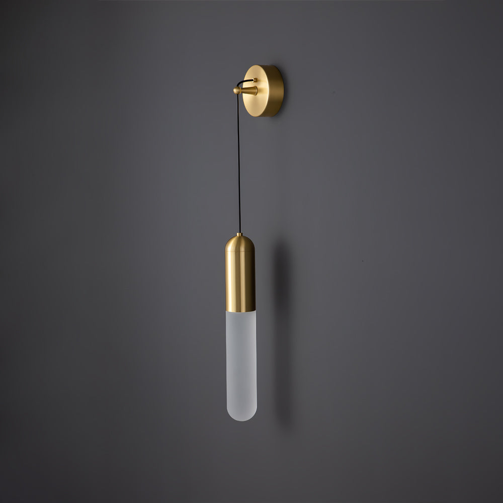 Unlit brass Clérachic wall light on a dark grey wall, the slim frosted cylinder shade pale and the brass cap and wall plate catching the light.