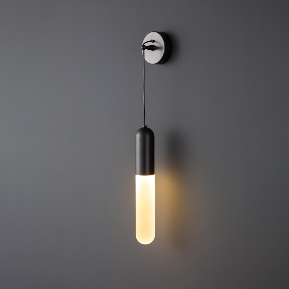 Black Clérachic wall light with a warm glow on a mid-grey wall, a slim cylinder shade hanging from a small wall plate.