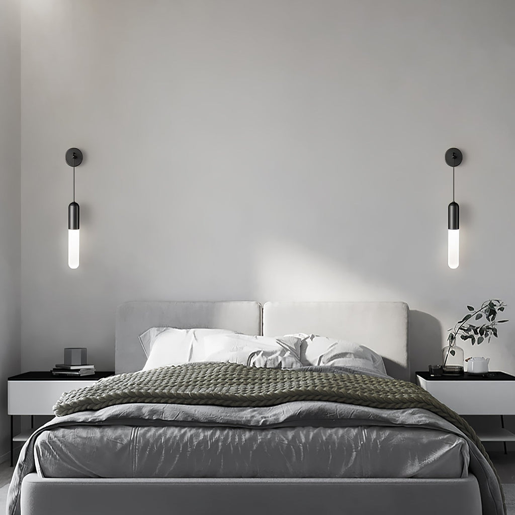 A pair of black Clérachic wall lights, one each side of a bed with a grey headboard, grey bedding and two black bedside tables.