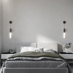 A pair of black Clérachic wall lights, one each side of a bed with a grey headboard, grey bedding and two black bedside tables.