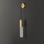 Unlit brass Clérachic wall light on a charcoal wall, the pale frosted cylinder shade hanging on a thin black cord.
