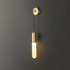 Brass Clérachic wall light on a dark wall, the slim cylinder shade lit warm and casting a soft amber glow on the wall beside it.