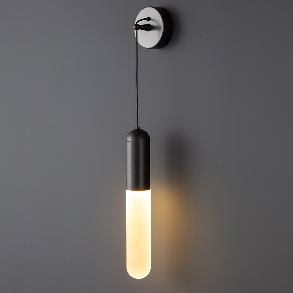 Close view of a black Clérachic wall light on a grey wall, its slim shade glowing warm below a silver-edged wall plate.