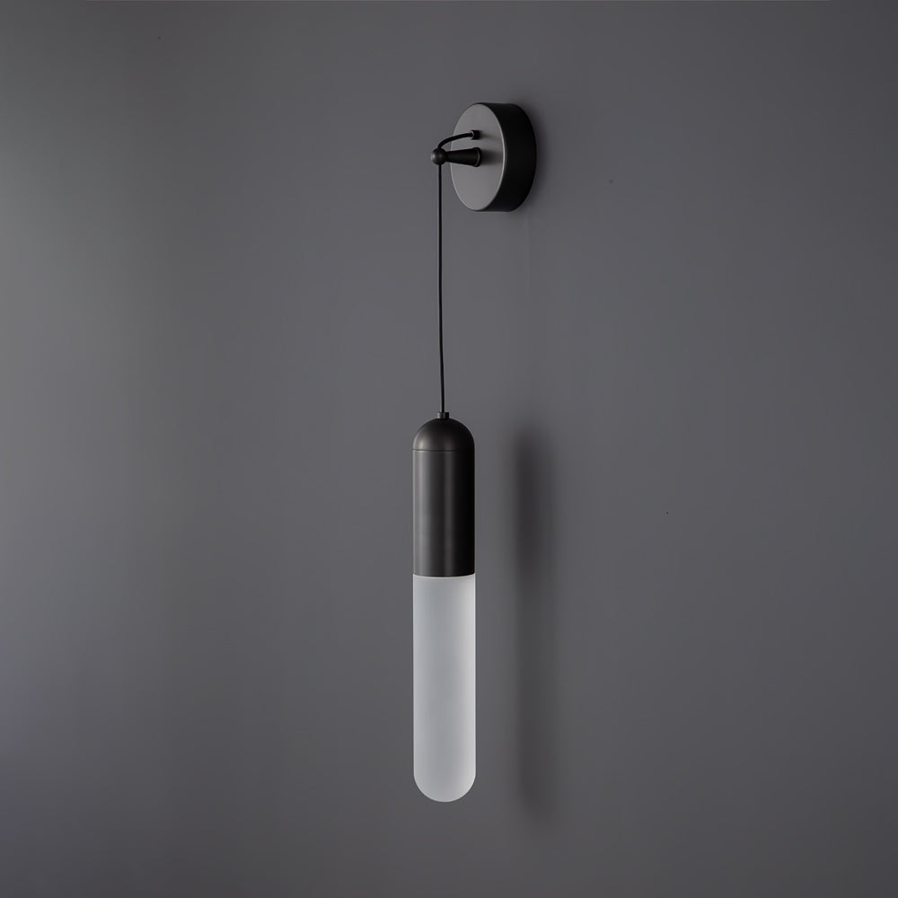Unlit black Clérachic wall light on a dark grey wall, the frosted cylinder shade pale beneath a black cap and wall plate.