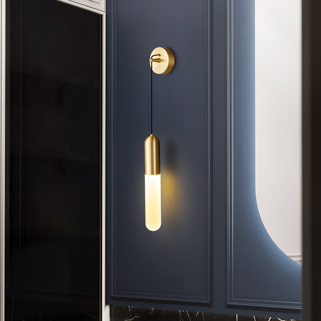 Brass Clérachic wall light on a navy panelled wall beside a dark glass door, its slim shade lit warm and a curved mirror glowing nearby.