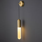 Brass Clérachic wall light on a dark grey wall, the cylinder shade glowing warm and casting a faint shadow to the right.