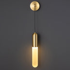 Brass Clérachic wall light up close on a dark grey wall, the round brass plate above a lit cylinder shade with a bright warm glow.