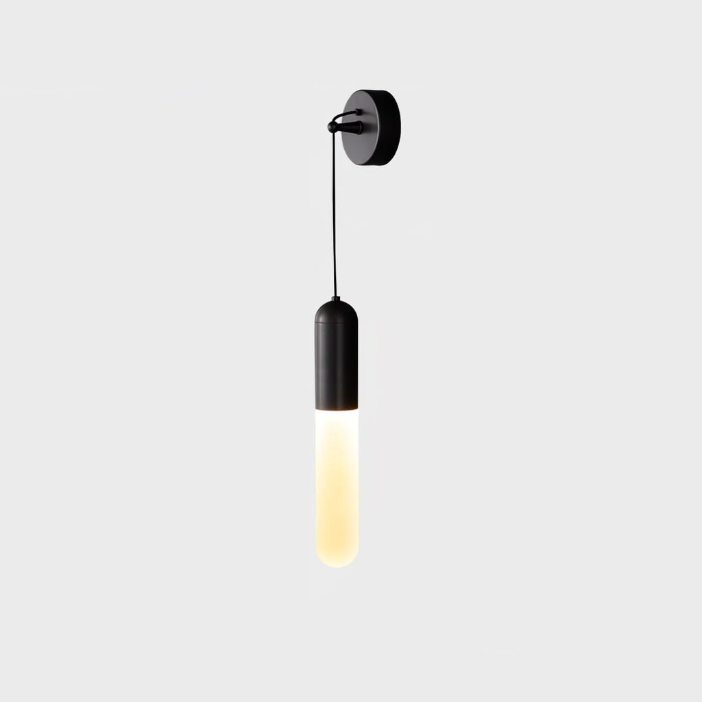 Black Clérachic wall light on a pale grey backdrop, a slim cylinder shade lit warm and hanging from a black wall plate on a cord.