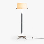 This Clérachic floor lamp has a cream fabric drum shade, a slim dark stem and a brushed metal star base, with a cord and foot switch.