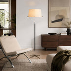Next to a low walnut sideboard and a steel-framed lounge chair, a Clérachic floor lamp stands tall on a woven rug.