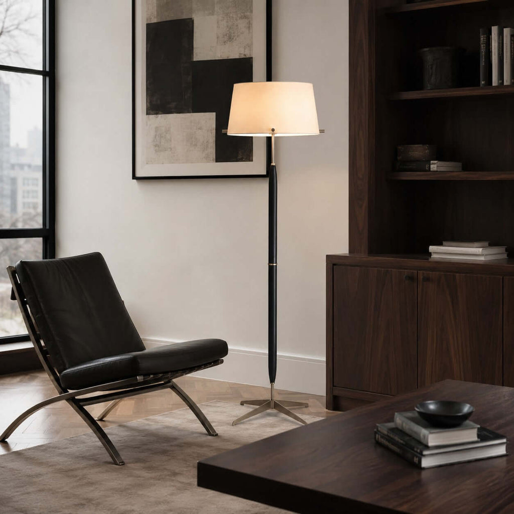 Beside a black leather lounge chair, a Clérachic floor lamp glows under a large abstract print, next to a dark wood bookcase.