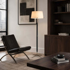 Beside a black leather lounge chair, a Clérachic floor lamp glows under a large abstract print, next to a dark wood bookcase.
