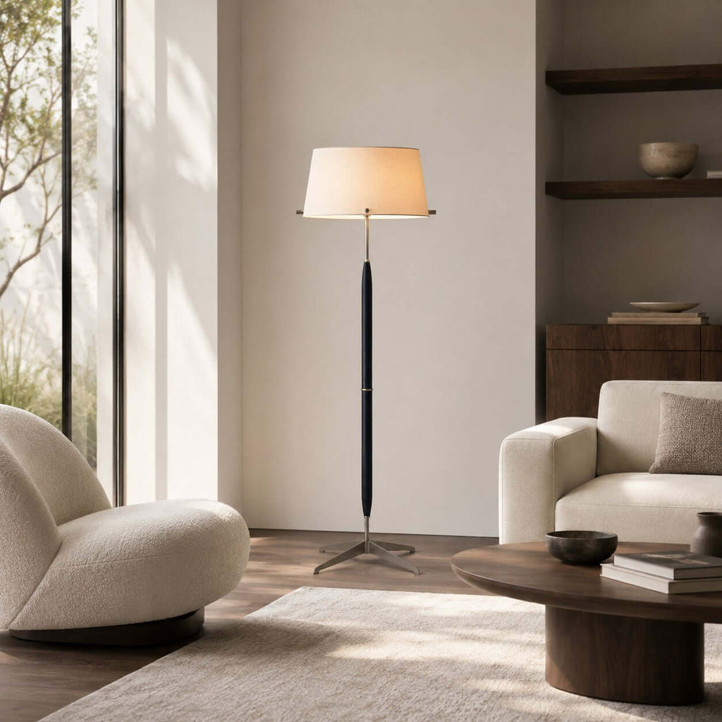 A Clérachic floor lamp stands between a curved cream armchair and a sofa, with a low round wooden table in front.