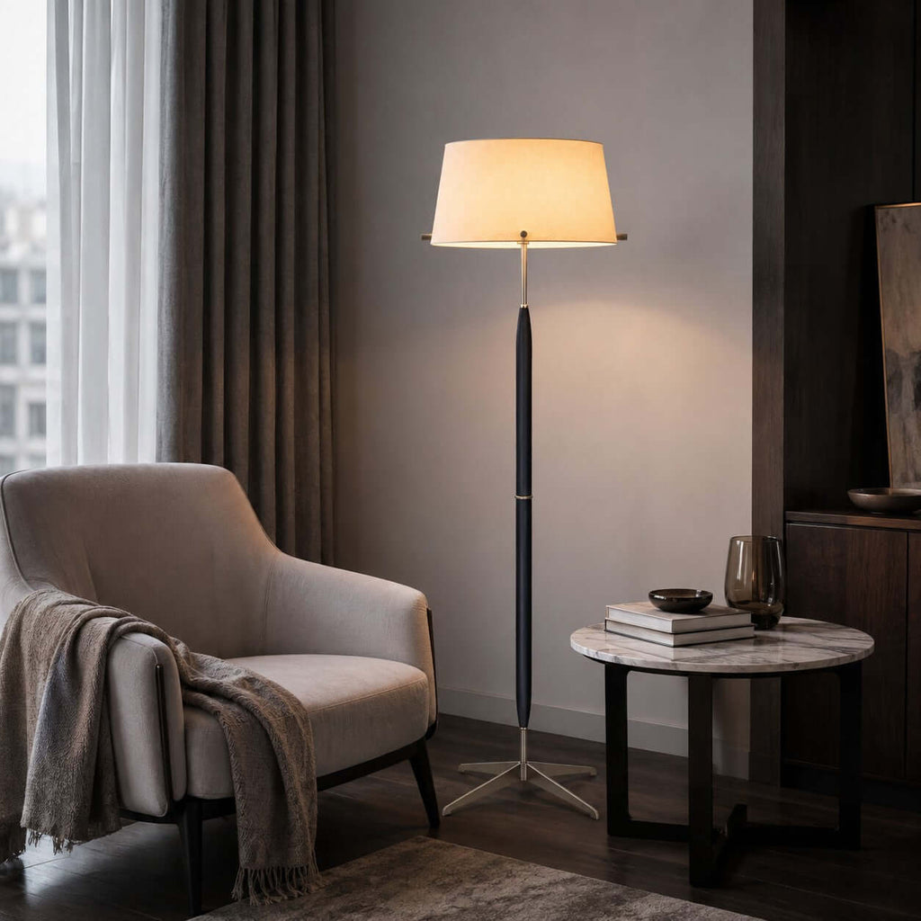A lit Clérachic floor lamp stands by a soft pink armchair with a grey throw, with a small round marble side table next to it.