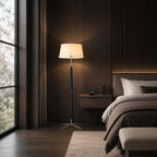 In a dark bedroom with slatted wood walls, a Clérachic floor lamp glows beside a window, a bed and a floating nightstand.