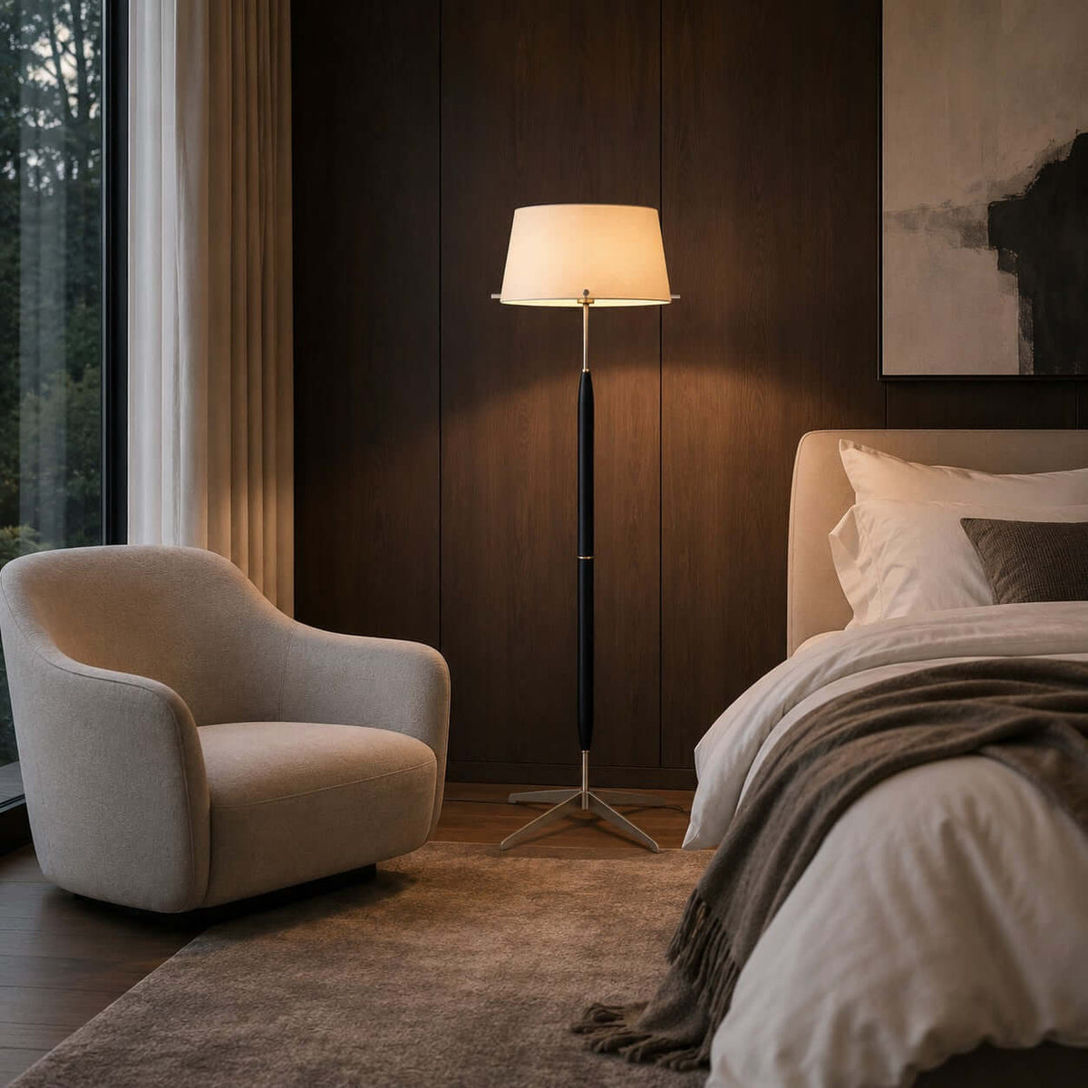 A Clérachic floor lamp stands between a cream curved armchair and a bed with a brown throw, against dark wood panelling.