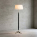 Alone in a concrete-walled room, this Clérachic floor lamp shows its cream drum shade, slim dark stem and star-shaped metal base.