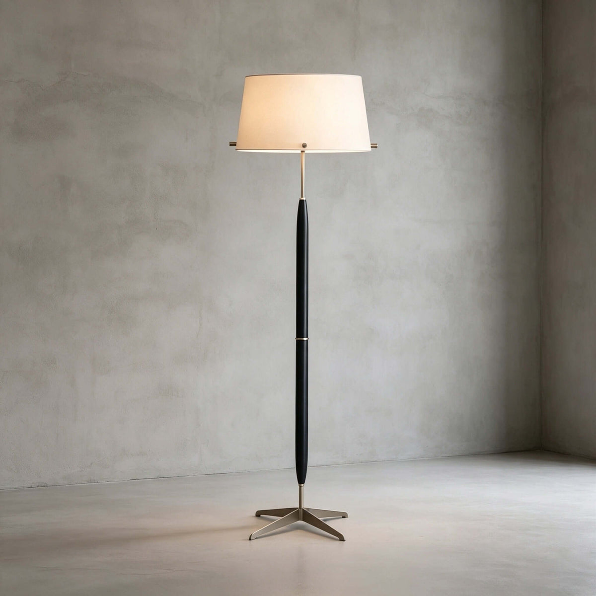 Alone in a concrete-walled room, this Clérachic floor lamp shows its cream drum shade, slim dark stem and star-shaped metal base.