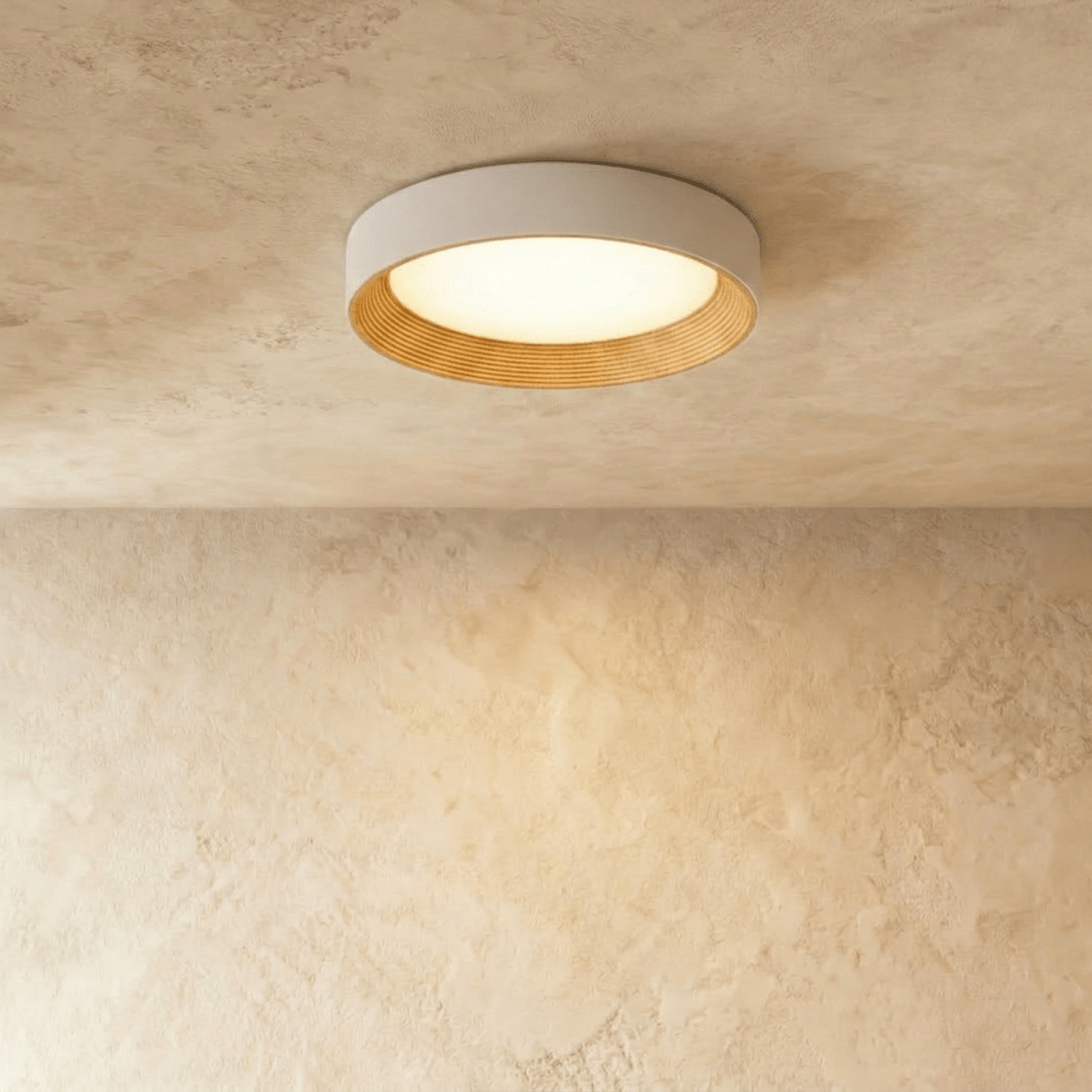 Clérachic round flush ceiling light with a pale rim and light wood-grain inner ring, glowing warm on a plaster ceiling.
