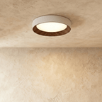 Clérachic round flush ceiling light with a pale rim and dark walnut-toned ribbed inner ring, lit on a plaster ceiling.