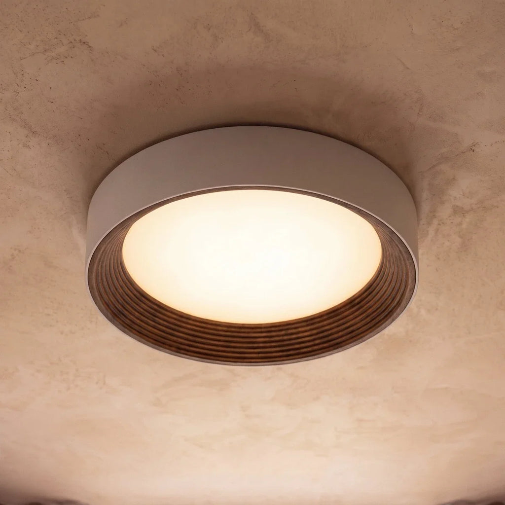 Clérachic round flush ceiling light seen from below, its lit diffuser framed by a ribbed dark walnut-tone inner ring.