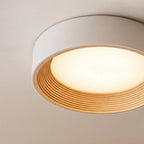 Clérachic close view of a round flush ceiling light, its pale rim, ribbed light wood ring and opal diffuser glowing warmly.