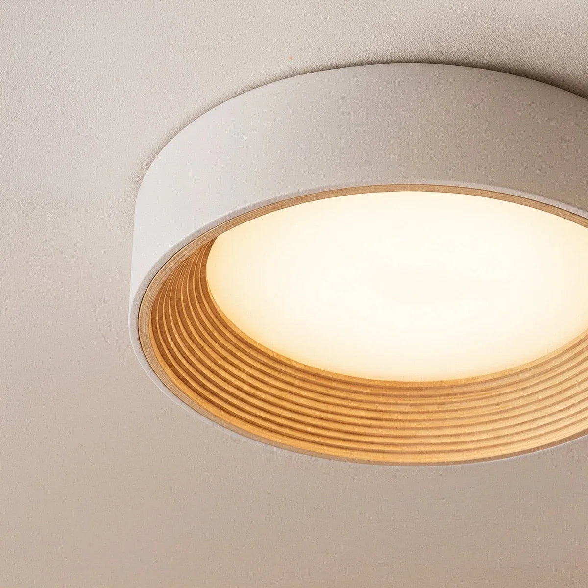 Clérachic close view of a round flush ceiling light, its pale rim, ribbed light wood ring and opal diffuser glowing warmly.