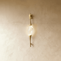 Clérachic slim gold wall light with a clear crystal centrepiece, glowing softly on a warm limewashed wall.