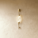 Clérachic slim gold wall light with a clear crystal centrepiece, glowing softly on a warm limewashed wall.