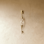 Clérachic slim gold wall light with a clear crystal centrepiece and tapered brass-tone ends, switched off on a limewashed wall.
