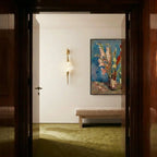 Clérachic gold wall light with a crystal centrepiece on a white hallway wall, beside a framed floral painting and a bench.